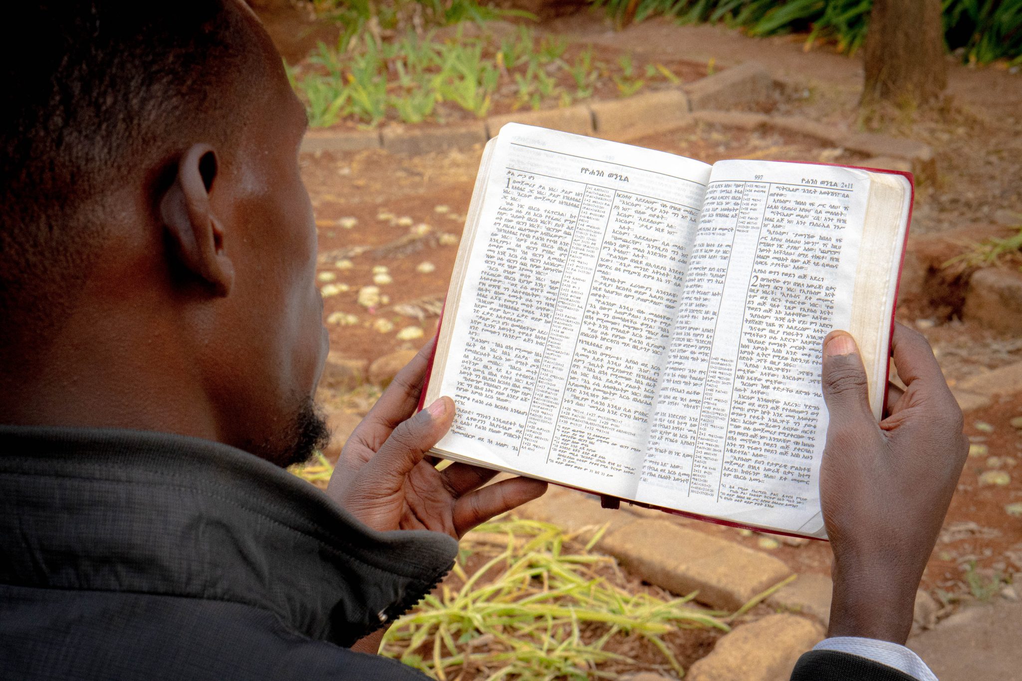 Kuva on Danielin olan takaa. Daniel pitelee amharankielistä Raamattua käsissään ja lukee sitä.