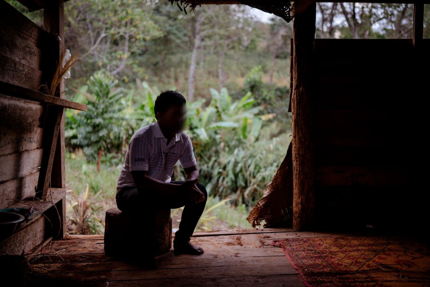 Mies istuu puupölkyllä puisen rakennuksen sisällä, miehen takana rakennuksen oviaukko ja taustalla viidakkoa.