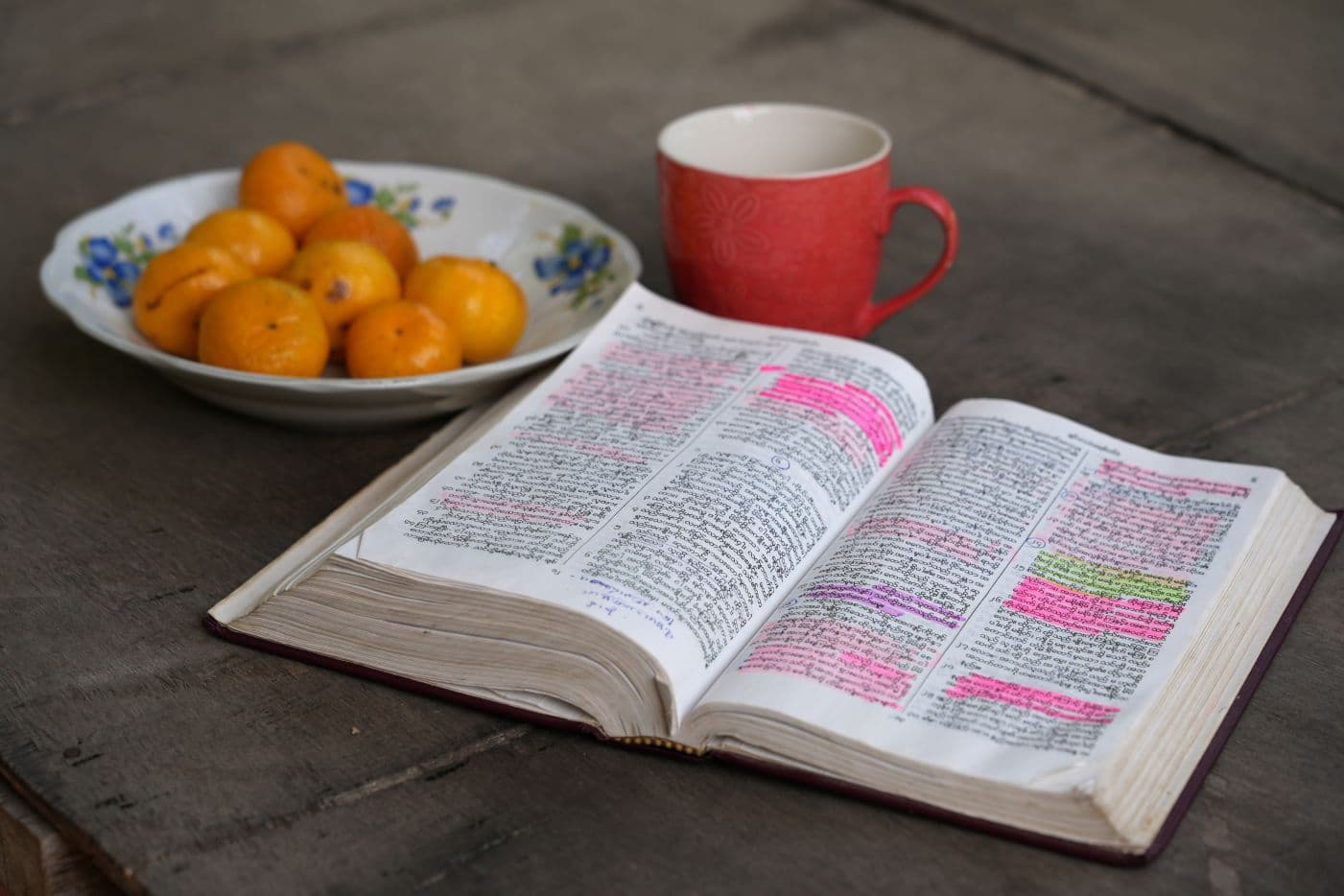 Avonainen Raamattu, kahvikuppi ja kulho, jossa on mandariineja.