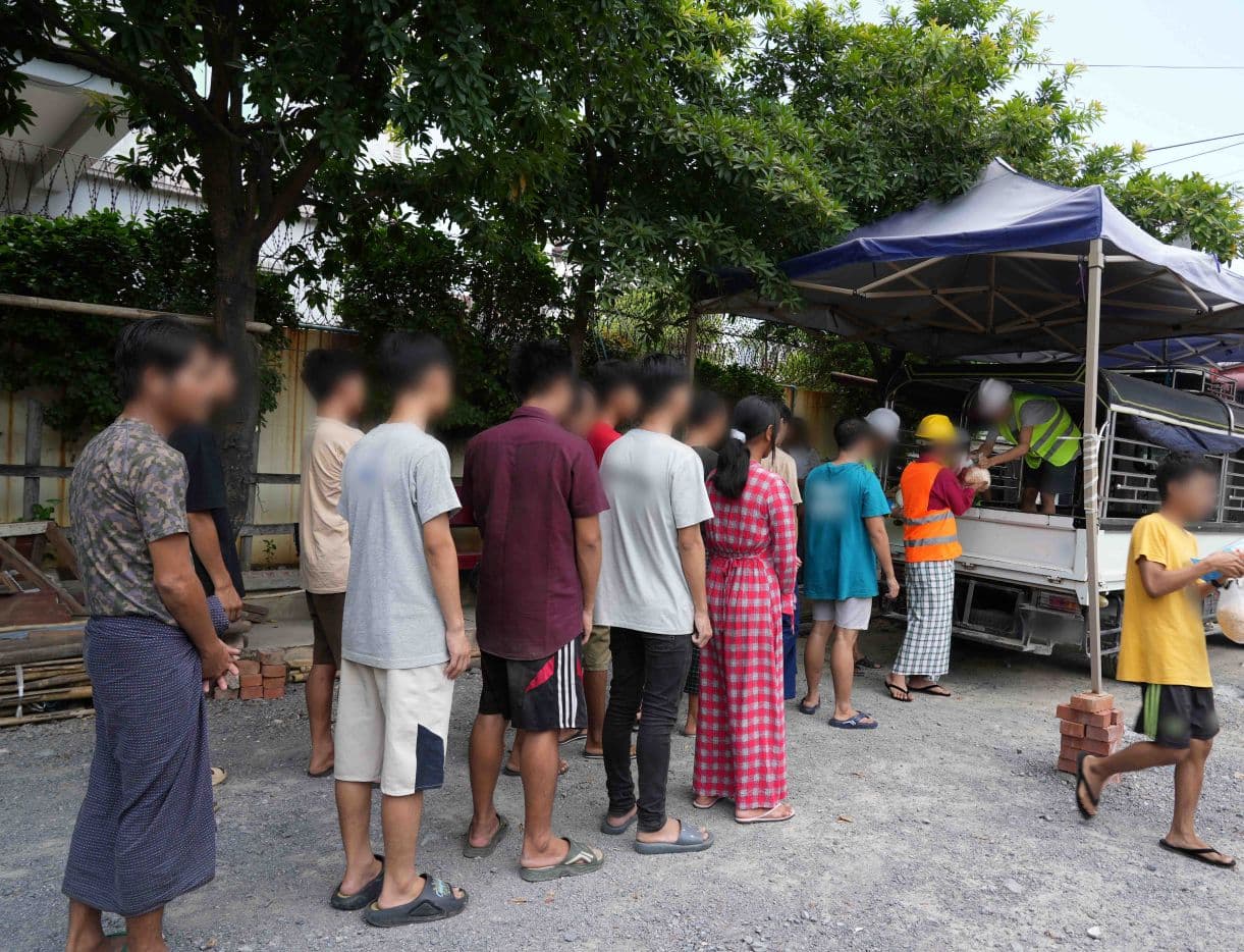 Ihmisiä jonottamassa auton peräkontille, jossa huomioliivinen mies jakaa heille pussukoita.