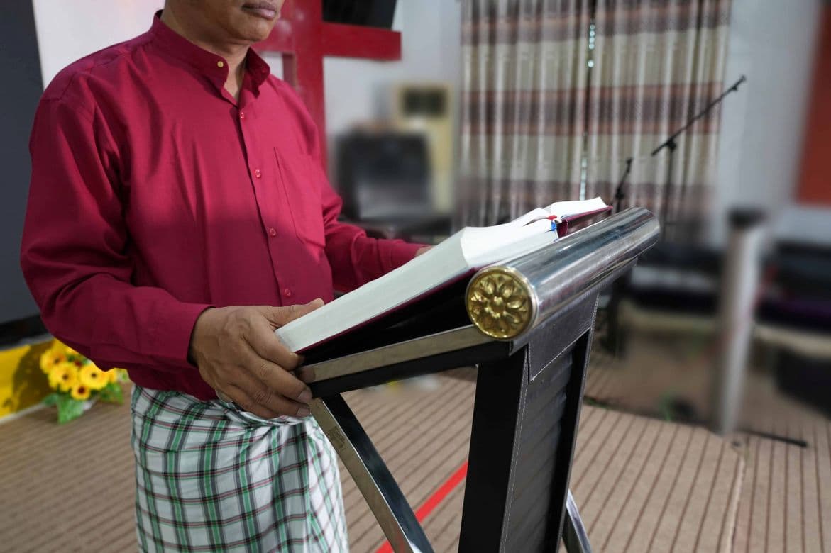 Mies puhujapöydän takana, puhujapöydällä avoin kirja.