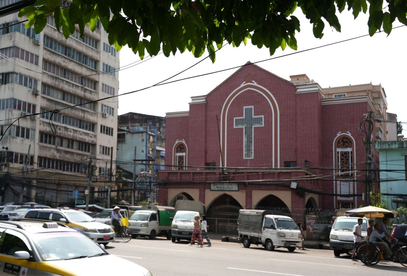 Punatiilinen kirkkorakennus kadun varressa, kadulla autoja, taustalla rähjäisen näköisiä kerrostaloja.