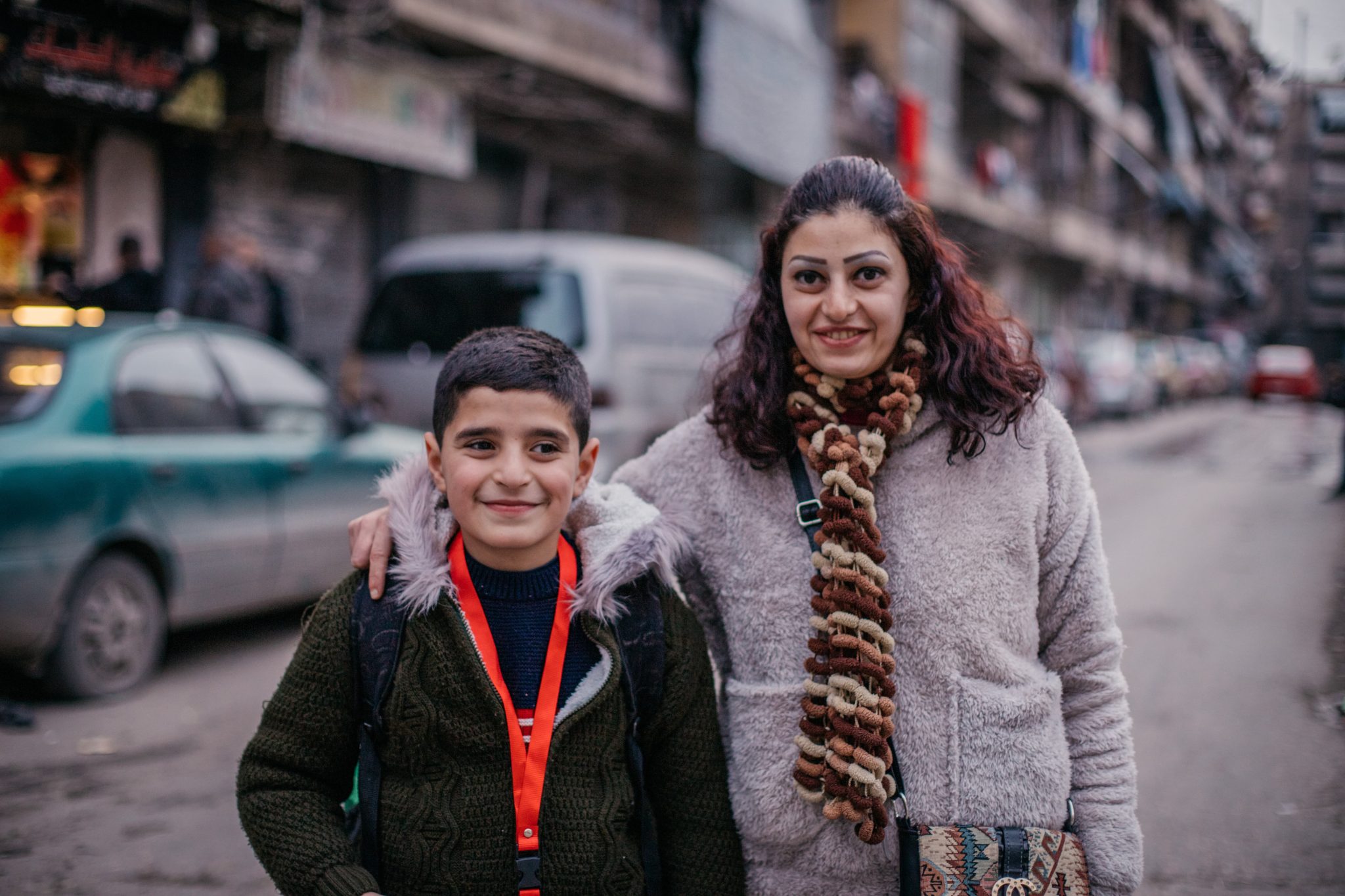 Syyrialainen äiti ja poika seisovat keskellä katua kerrostalojen edessä.