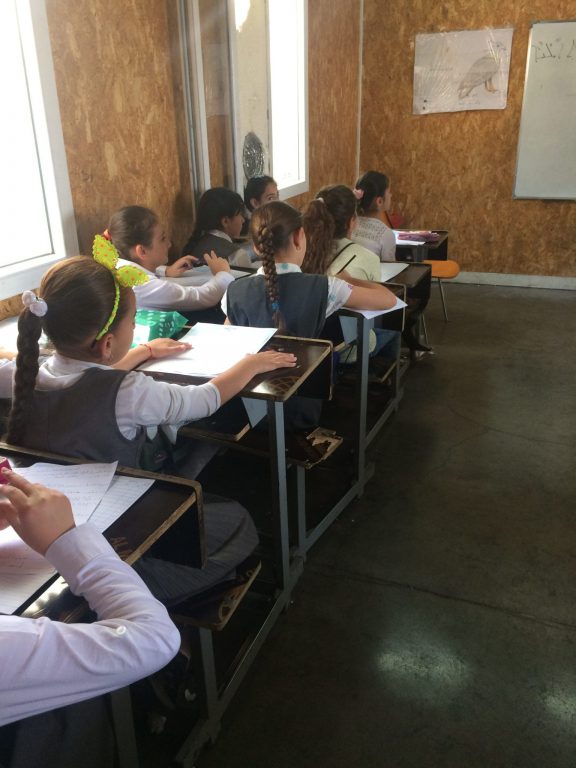 Lähi-idässä koululaisia pulpettien ääressä luokkahuoneessa. Kuva otettu luokkahuoneen takaosasta.