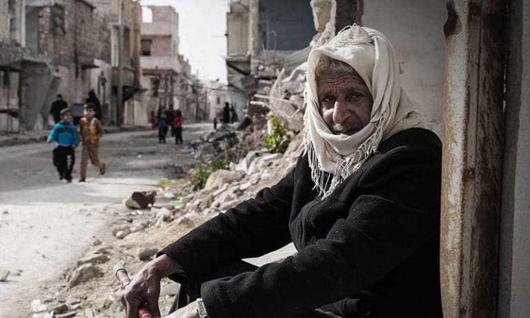 Syyrialainen mies istuu kadun laidalla sodassa tuhoutuneiden rakennusten keskellä