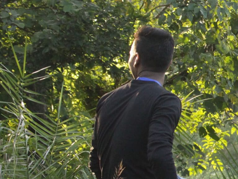 Vainottu Intialainen nuorimies istuu kasvillisuuden keskella kasvot käännettynä pois