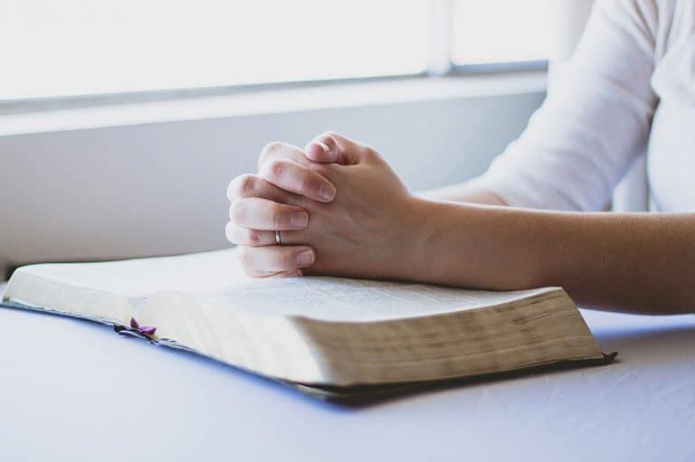 Kädet ristissä rukouksen merkiksi pöydällä Raamatun päällä