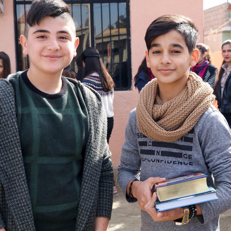Kaksi poikaa hymyilee kameralle, toisella heistä kuvitettu Raamattu ja toinen kirja käsissään.