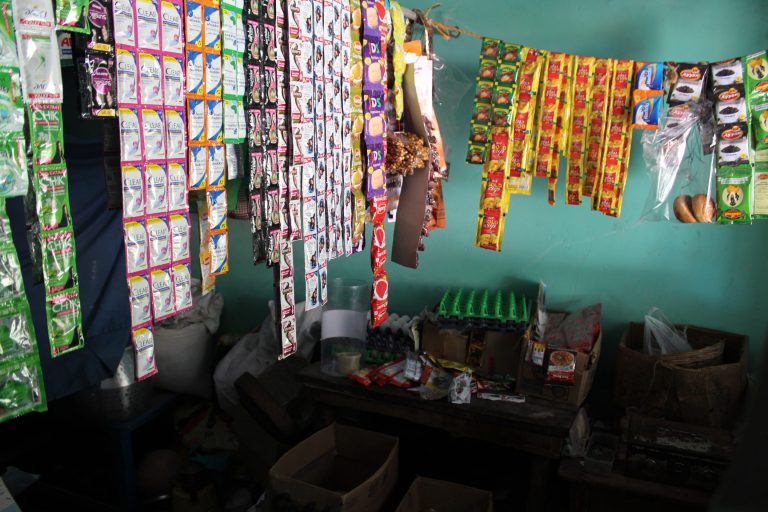 Kuva on Ramin kotona olevasta kaupasta. Narun varassa roiikkuu erilaisia myyntituotteita, pienissä värikkäissä pusseissa. Lattialla näkyy pahvilaatikoita.