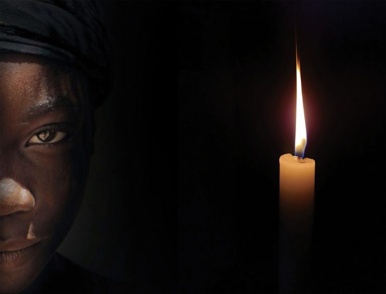 Afrikkalaistaustainen nainen katsoo intensiivisesti kameraan, vieressään korkealla liekillä palava kynttilä