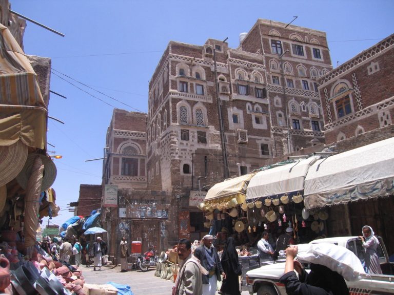 Kuva Jemeniläiseltä kadulta. Yläosassa näkyy rakennuksia, alaosassa kauppiaiden kojuja.