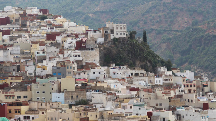 Kuvassa rinteellä oleva marokkolainen kaupunki. Takana toinen vuoren rinne, jolla kasvillisuutta.
