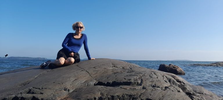 Kuvassa Ulrika istuu rantakallion päällä. Hänellä on mustat aurinkolasit ja vaalea tukka.