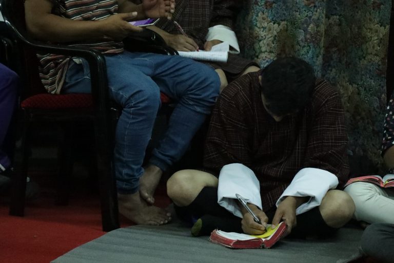 Tummasävyinen kuva kahdesta bhutanilaisesta kristitystä, jotka lukevat Raamattua kotikokouksessa.