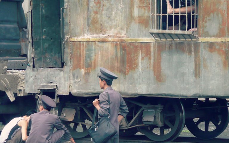 Kuvan etualalla pohjoiskorealaisia sotilaita, takana junan vaunu, jossa kaltereiden takaa näkyy jalat.
