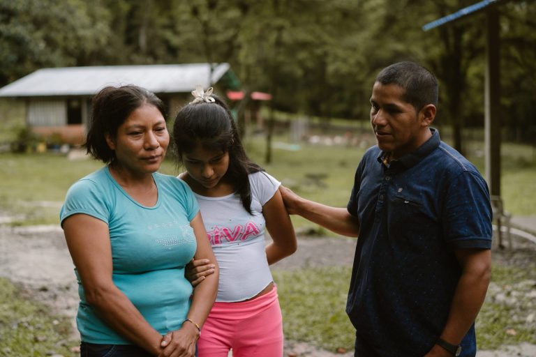 Kolumbialainen perhe seisoo toisiinsa tukeutuen pihamaalla.