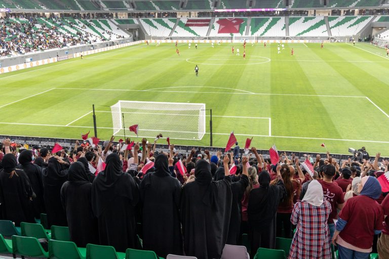 Peittäviin asuihin pukeutunut qatarilainen katsojajoukko jalkapallostadionilla seuraamassa ystävyysottelua.