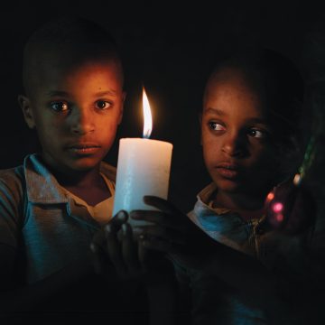 Kaksi etiopialaista poikaa pitävät käsissään palavaa kynttilää pimeässä