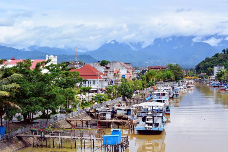 Sumatralla kaupunkia halkova joki, jossa veneitä. Taustalla kohoaa vuoria.