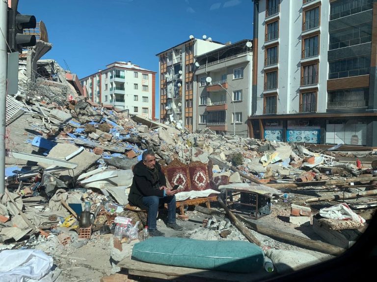 Mies istuu kerrostaloalueella romahtaneen talon raunioilla.