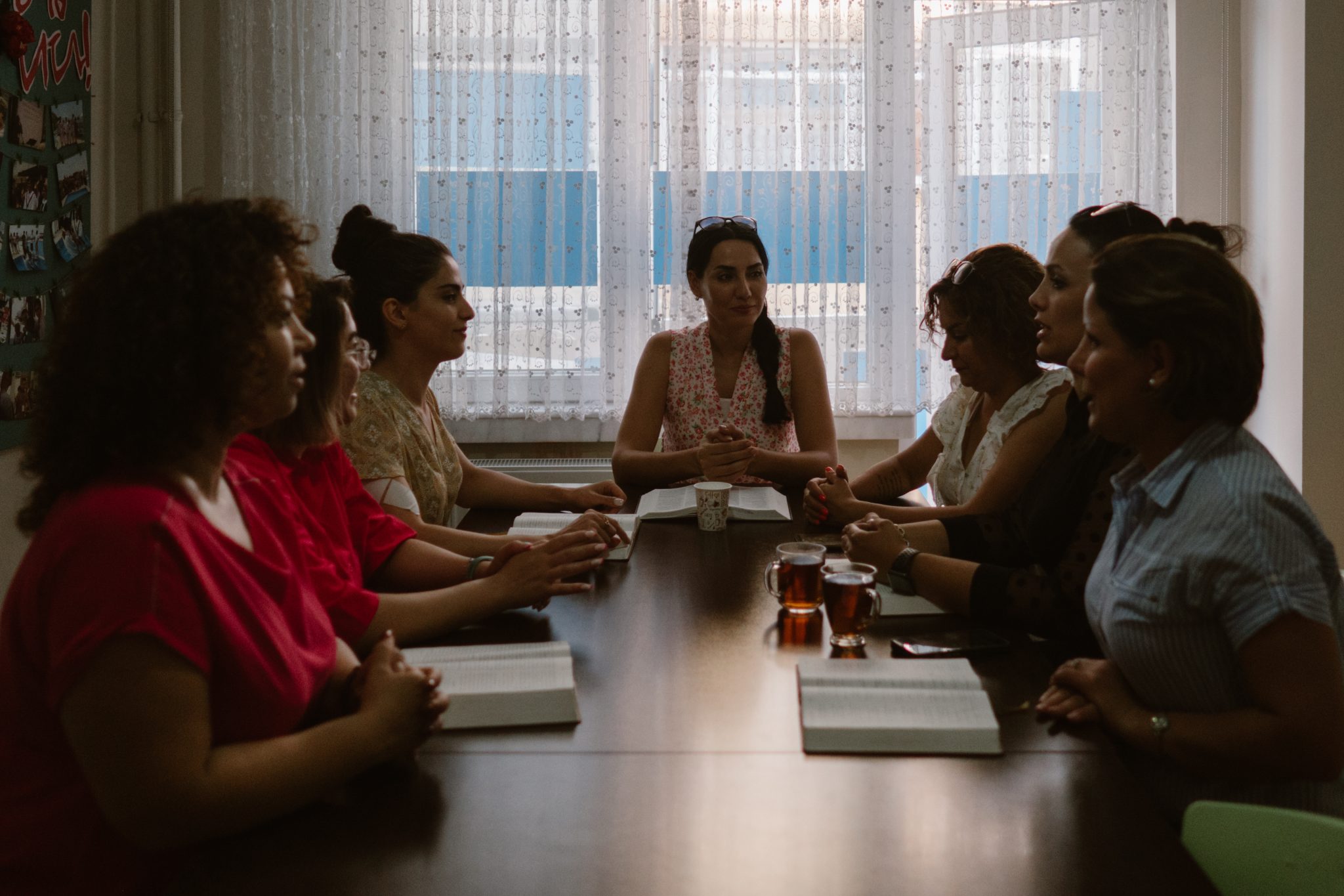 Naisia pöydän ympärillä kokoontuneina raamattupiiriin hämärässä kuvassa.