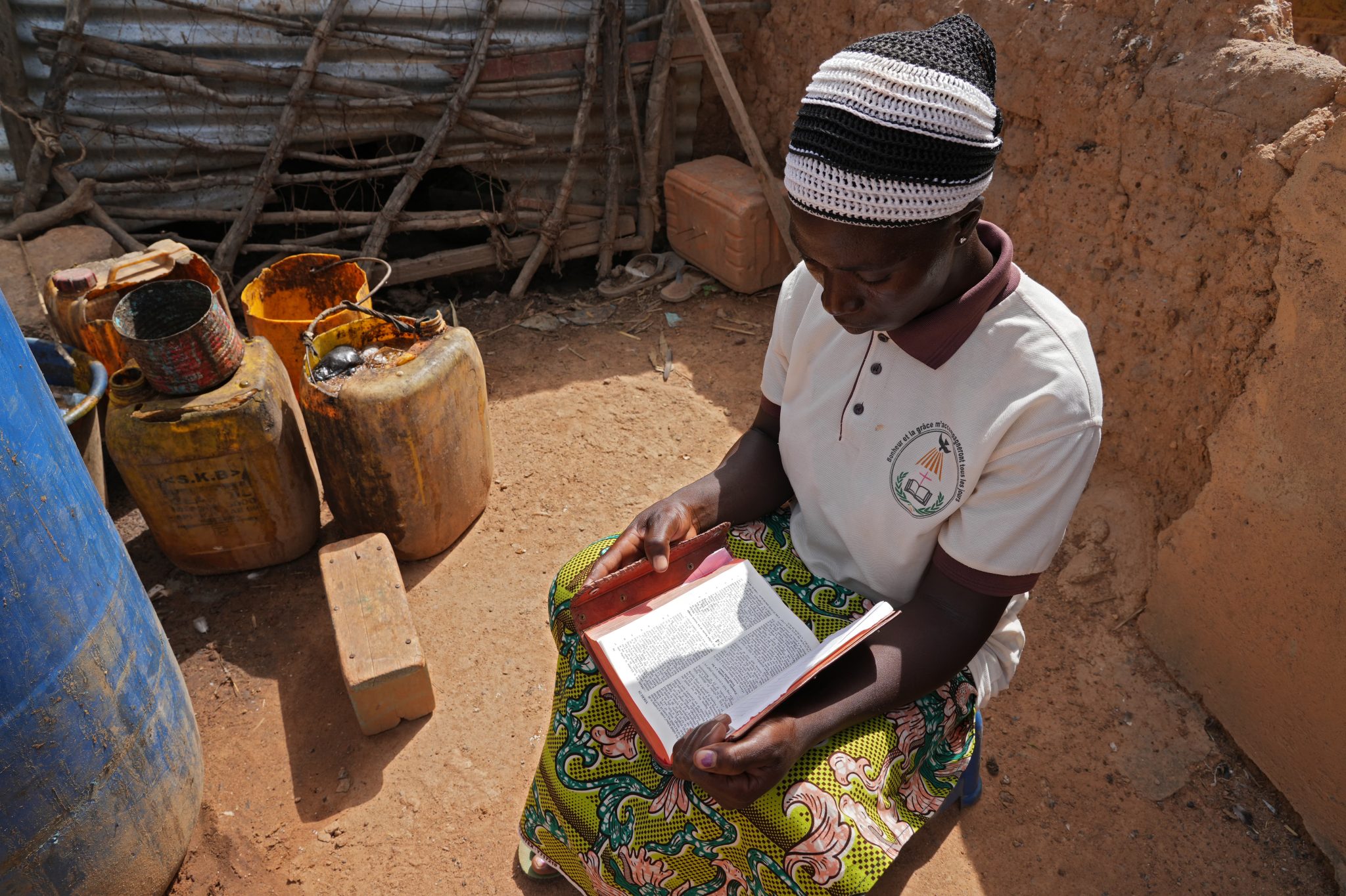 Afrikkalainen nainen istuu pihalla lukemassa Raamattua.