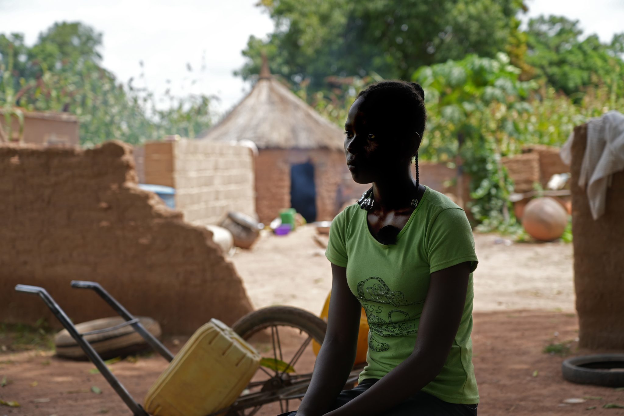 Hoikka afrikkalainen nuori nainen istumassa kotinsa edessä kasvot tummennettuina.