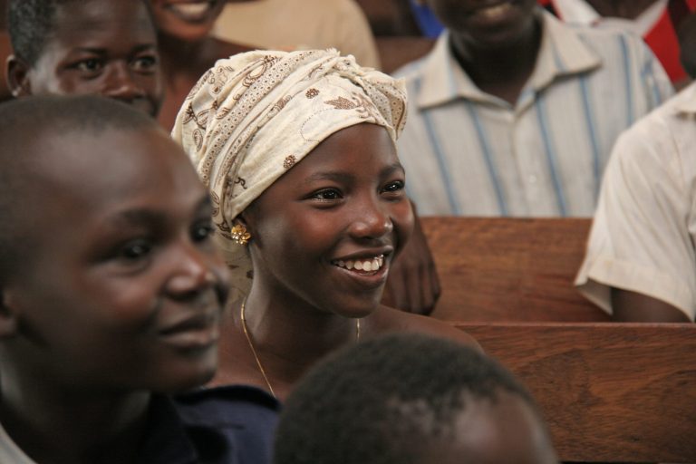 Huivipäinen nuori tyttö kirkonpenkissä muiden lasten ympärillä Afrikassa.