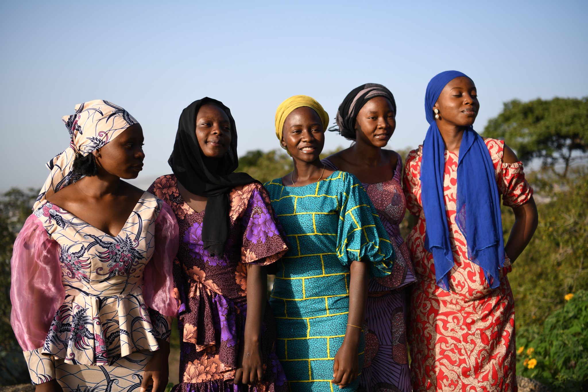Hymyileviä, värikkäisiin mekkoihin ja huiveihin pukeutuneita afrikkalaisia naisia rivissä.