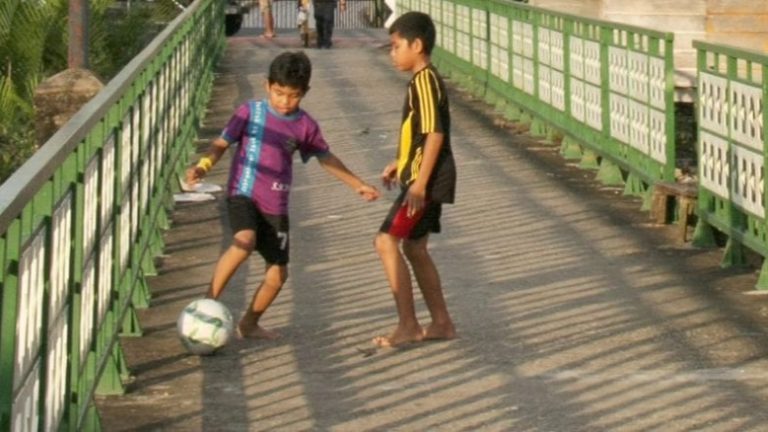 Kaksi poikaa pelaa palloa kaiteiden välissä