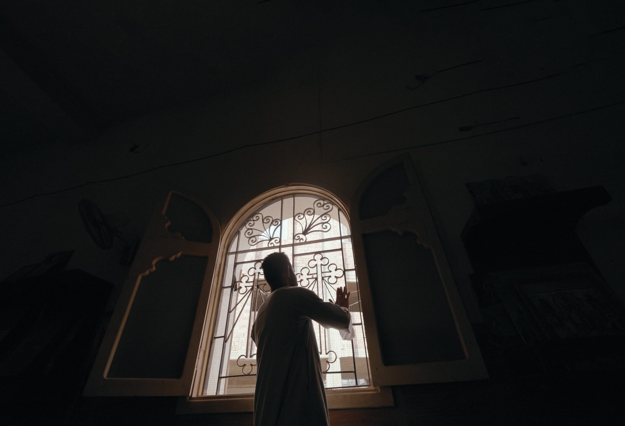 Mies seisoo koristeellisen ikkunan edessä pimeässä huoneessa.