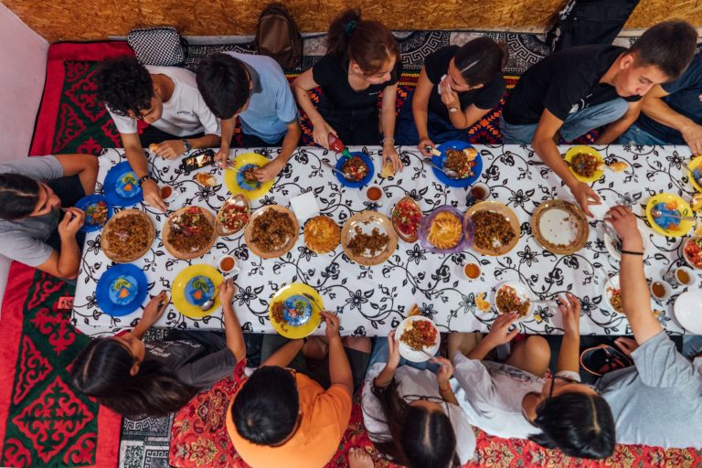 Ylhäältä otettu kuva nuorista ihmisistä keskiaasialaisessa ruokapöydässä