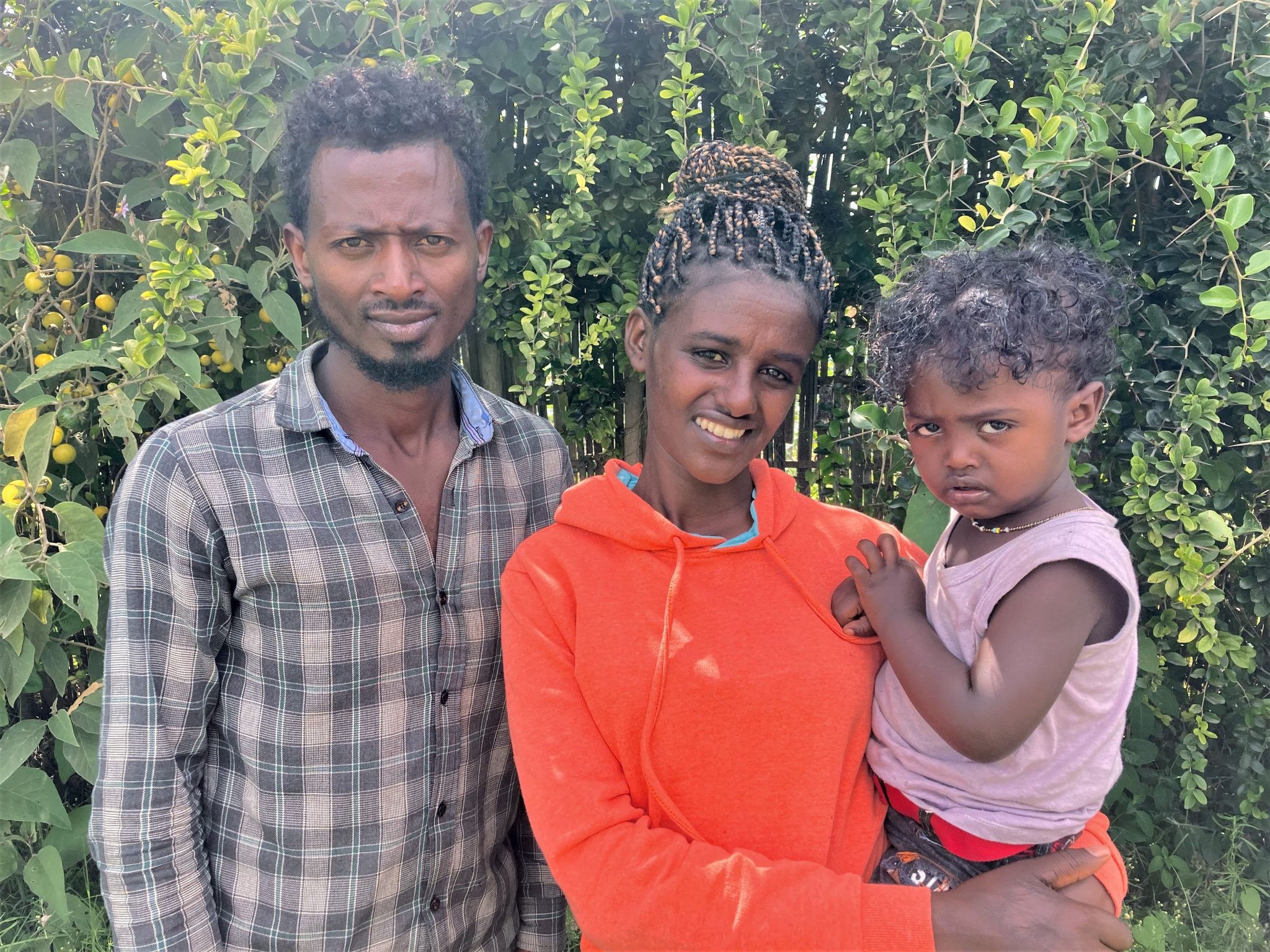 Etiopialainen perhe hymyilee ja katsoo kameraan. Mies, nainen ja naisen sylissä pieni poika.