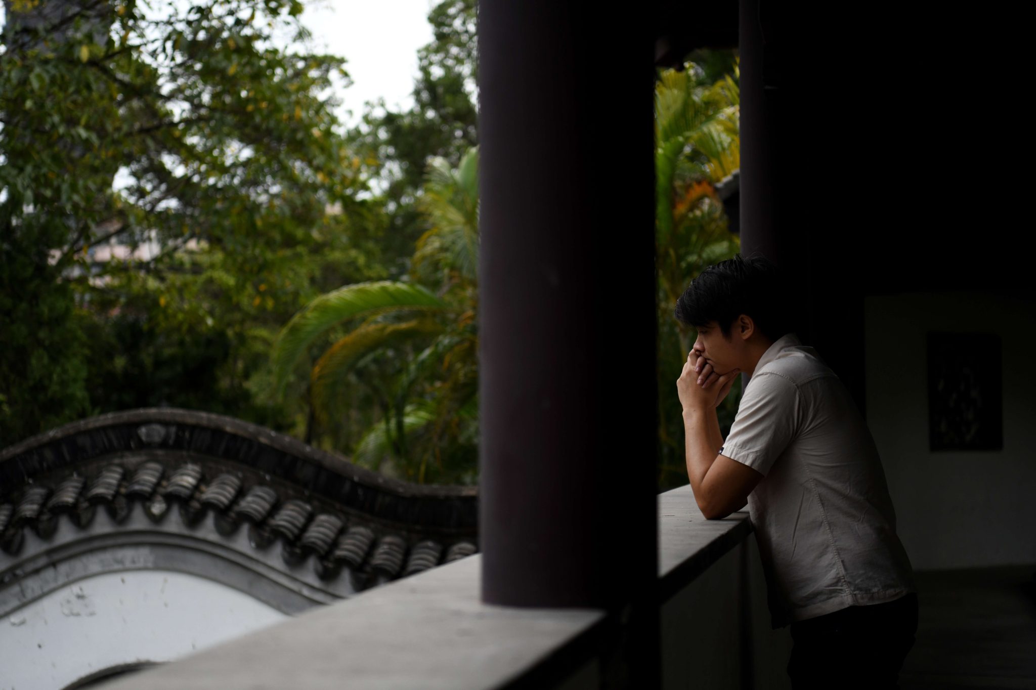 Mies seisoo kiinalaisessa puutarhassa rakennuksen varjossa.