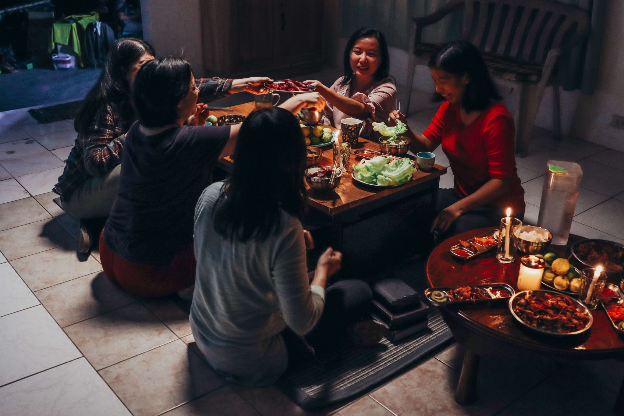 Viisi naista kokoontunut syömään matalan pöydän ympärille hämärähkössä tilassa