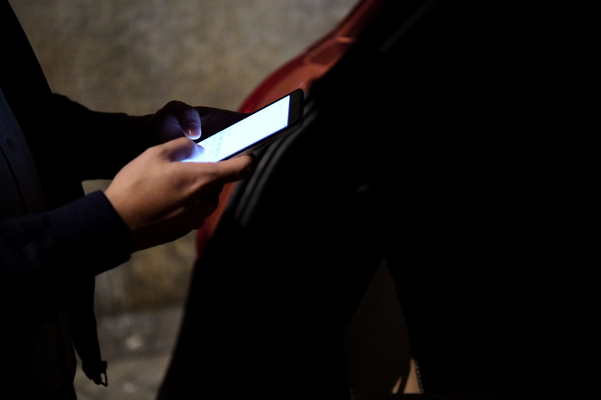 Pimeä kuva henkilöstä katsomassa puhelinta auton takaluukun luona.