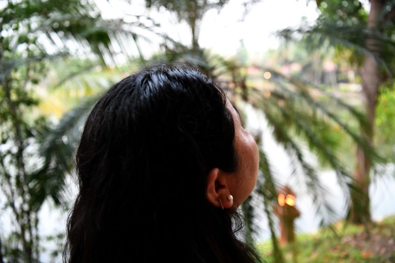 Tummatukkainen nainen kuvattuna takaapäin palmujen alla.
