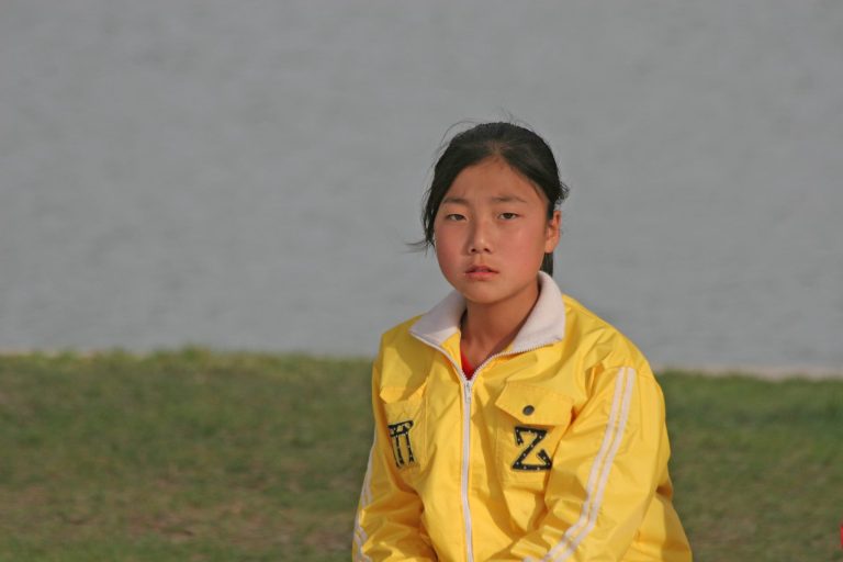 Vakavailmeinen nuori tyttö istuu ulkona keltainen takki päällä.