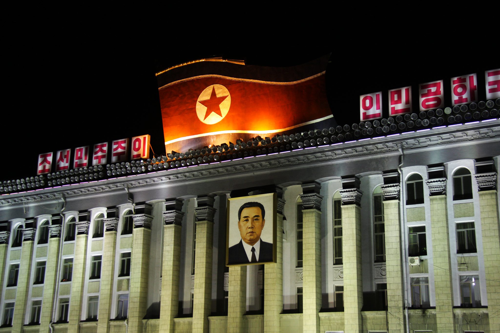 Valaistu hallintorakennus, jonka katolla valtava Pohjois-Korean lippu.
