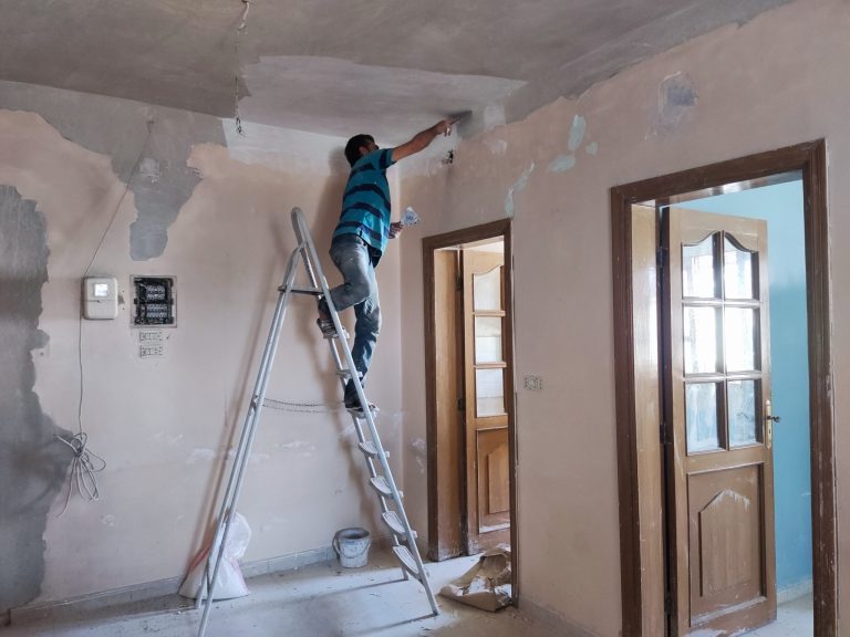 Mies tikkailla korjaamassa sisäkattoa vaurioituneessa kodissa
