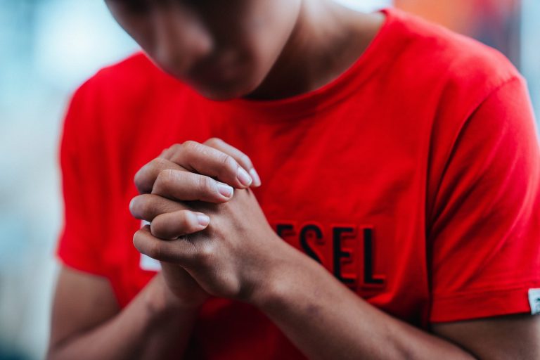 Nuori poika punaisessa t-paidassa rukoilemassa