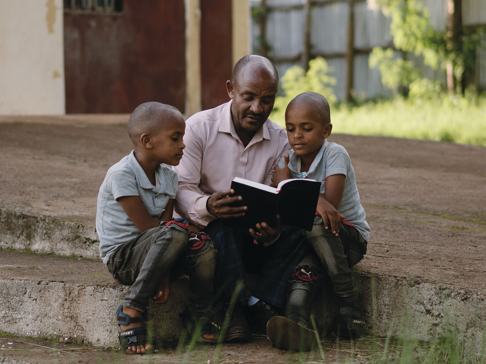 Etiopialainen isä lukee kaksospojilleen ensimmäisen Joulun tapahtumista ulkona istuen