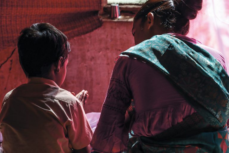 Intialaispoika rukoilee äitinsä kanssa istuen, kasvot kuvasta poispäin