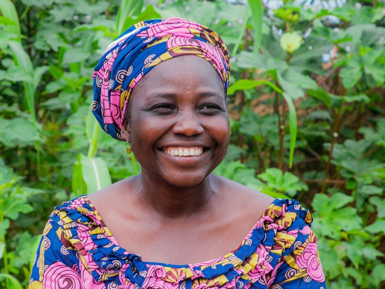 Nigerialaisnainen hymyilee leveästi taustalla vehreää kasvillisuutta