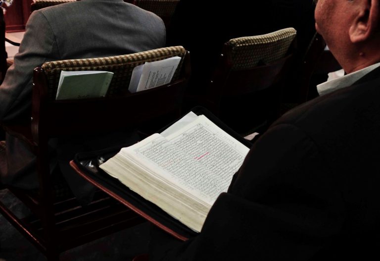 Takaviistosta kuvattu mies istuu avoin Raamattu sylissään.