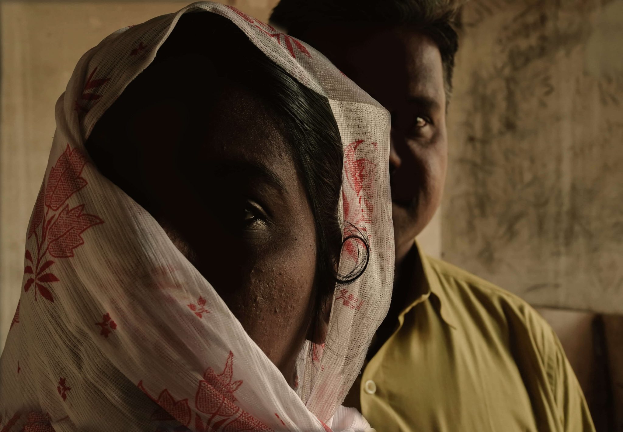Intialainen nainen kasvot osittain huivilla peitettynä, naisen pään takaa näkyvät osittain miehen kasvot.