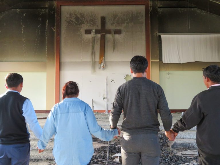 Ihmisiä käsi kädessä tuhotussa kirkossa.