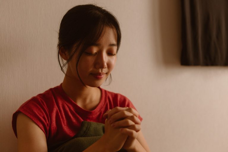 Aasialainen nuori nainen rukoilee silmät kiinni ja kädet ristissä.