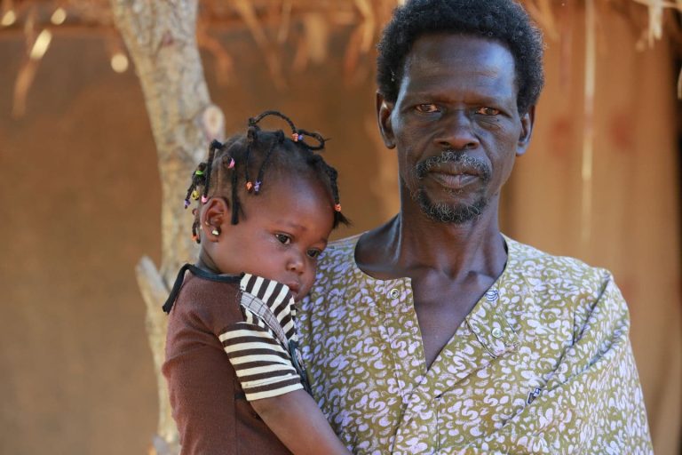 Valokuva afrikkalaisesta miehestä pieni lapsi sylissään.