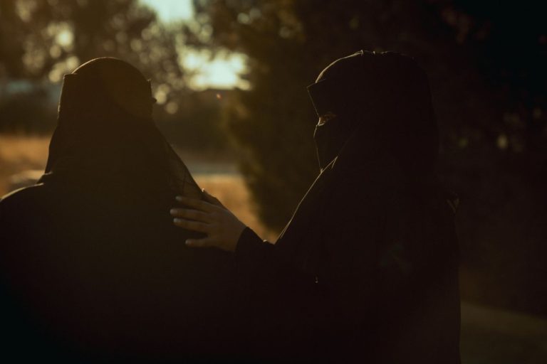 Kaksi burkaan pukeutunutta naista selin kameraan.